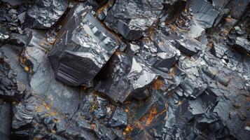 Shiny black mineral rocks with sharp edges are featured in a close up view, highlighting their unique textures and vibrant orange hues among black surfaces in natural light. photo