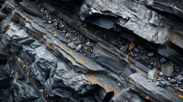 Close up view of unique rock layers highlighting the contrast between dark minerals and patches of orange lichen, illustrating geological processes in a natural setting under sunlight. photo