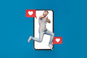 A young person joyfully jumps in front of a smartphone, surrounded by heart icons and text bubbles. This vibrant display captures the excitement of digital connections and modern dating. photo