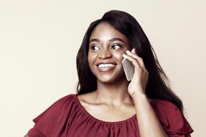 Happy young black lady in casual outfit having phone conversation with boyfriend or bestie, smiling and looking at copy space for advertisement on beige studio background, panorama photo
