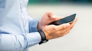 Unrecognizable businessman standing by office center, holding modern smartphone with blank screen, checking business process online, using mobile business application, closeup, copy space photo