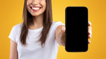 Mobile Application Ad. Portrait Of Happy Lady Showing Smart Phone Black Empty Screen Recommending App Standing Over Yellow Orange Studio Background. Selective Focus On Cell Display, Check This Website photo