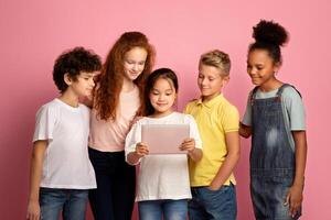 Multinational young students using tablet computer to study together on pink background photo