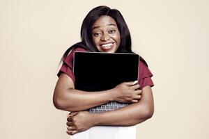 Delighted young african american woman hugging gadget and smiling, enjoying her brand new modern laptop, studio background, copy space. Computer, notebook, laptop, gadgets, modern technologies concept photo