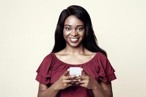 Positive young african american woman with newest cellphone looking at camera and smiling over beige studio background, using nice dating, entertaining mobile application on smartphone, copy space photo