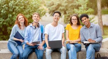 Happy Diverse Students Posing Sitting And Learning Together Using Laptop Computer Outside, Smiling To Camera. Education Concept photo