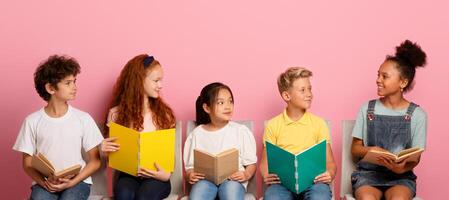 Back to school. Diverse children with notepads and books looking at each other while sitting on chairs over pink background photo