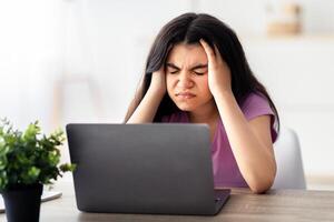 Exhausted Indian teen girl suffering from headache, having migraine, overworking, having too much online homework indoors. Tired adolescent facing difficulties studying remotely photo