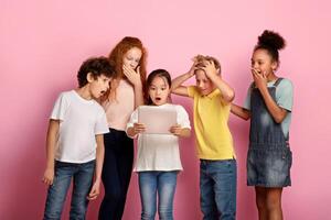 Group of shocked multiracial friends watching something on tablet computer together, pink background photo