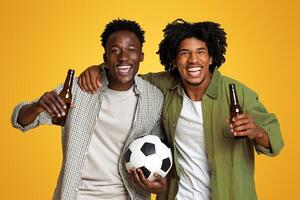 Football Fans. Two Cheerful Black Guys Holding Soccer Ball And Drinking Beer, Having Fun Together On Beige Background, Excited Happy African American Male Friends Cheering Favorite Team, Free Space photo