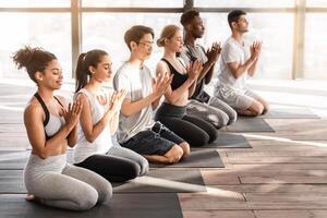 Yoga Lesson. Group of sporty young people doing lotus seal gesture, and meditating in studio together, side view with free space photo