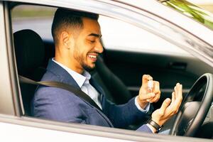 Cheerful businessman using disinfectant spray while sitting in car, handsome middle-eastern man in suit cleaning his hands after business meeting or working day, hygiene while coronavirus pandemic photo