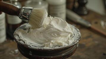 A hand gently swirls a shaving brush into a bowl of creamy white lather, preparing for a classic wet shave in an old fashioned grooming space filled with tools. photo