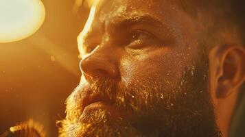 A man with a well groomed beard is captured in a concentrated expression, surrounded by warm lighting that highlights his features in a low lit environment. photo
