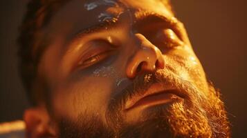 A man rests peacefully with his eyes closed, displaying a serene expression while receiving a calming treatment at a wellness center. The warm lighting enhances the tranquil mood. photo