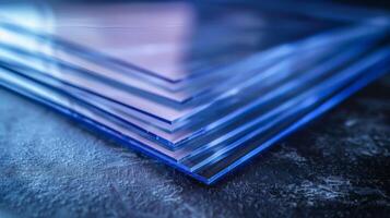 Transparent acrylic sheets are stacked in neat layers on a dark, textured surface, showcasing their clarity and modern design in a well lit space. photo