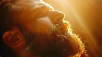 A man is basking in warm sunlight, allowing the golden rays to illuminate his face and beard, conveying a sense of peace and deep thoughtfulness. photo