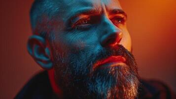 A man gazes thoughtfully with a textured beard and intense expression, illuminated by warm and cool lighting in an artistic atmosphere during the evening. photo