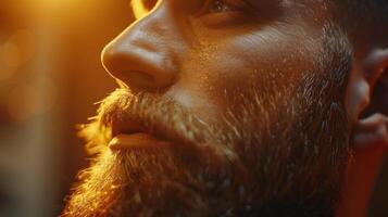 A man with a well groomed beard gazes thoughtfully to the side, with soft warm lighting creating a captivating atmosphere that enhances his facial features and expression. photo