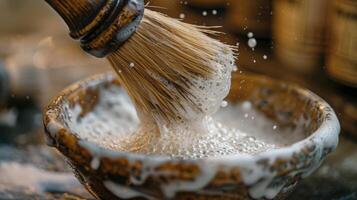 A shaving brush swirls in a rustic bowl, creating a thick, frothy lather. The ambient light highlights droplets of soap bubbles, enhancing the grooming atmosphere. photo