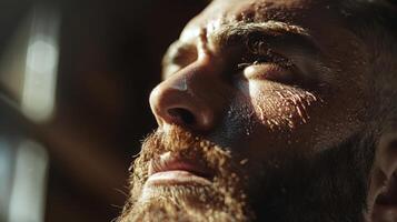 A man with a thick beard and intense gaze is illuminated by warm sunlight. He appears deep in thought, showcasing his facial features and texture. The atmosphere suggests contemplation and focus. photo