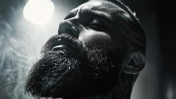 A man with an impressive beard and tattoos stands in a dimly lit environment, lost in thought as smoke wisps around him, creating an atmospheric, moody effect. photo