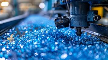 Large machine operates in a factory, producing and processing vibrant blue plastic pellets as part of a manufacturing process under bright industrial lights. photo