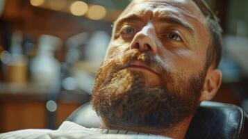 A man lies back in a barbershop chair, receiving a beard grooming treatment. The ambiance is warm and inviting, with tools and products visible in the background. photo