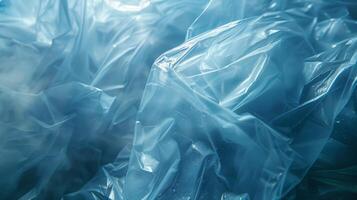Translucent blue plastic sheets are piled and wrinkled, reflecting sunlight and casting intricate shadows while revealing layers that suggest depth and texture in a natural environment. photo