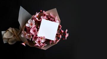 A bouquet of cherry blossom flower wrapped with a packet on dark background and a blank white greeting card is attached on it photo
