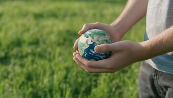 A person holding a small globe in a grassy field, symbolizing care for Earth. photo
