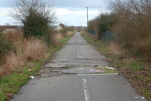 A cracked, overgrown road leading to a distant structure under cloudy skies. photo