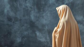 A figure draped in a beige garment stands against a textured backdrop. photo