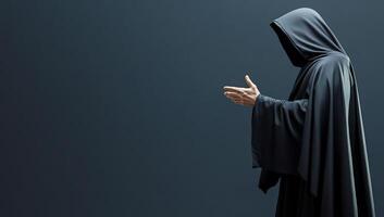 A cloaked figure gesturing in a dark, minimalist setting. photo