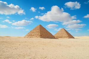 Two pyramids stand in a sandy desert under a blue sky with clouds. photo