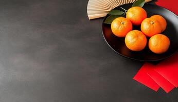 A black plate with oranges, red envelopes, and a fan on a dark surface. photo