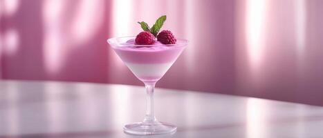 A vibrant dessert featuring layers of pink yogurt, topped with raspberries and mint, served in a stylish glass against a soft pink backdrop. photo