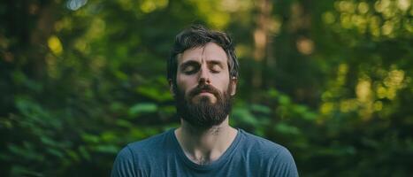 A serene man with a beard meditates in a lush, green forest, embodying tranquility and connection with nature. photo