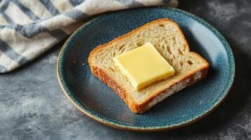 Fresh Slice of Bread with Butter on a Blue Plate and Striped Cloth in the Background photo