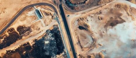 An aerial view of a landscape featuring winding roads, patches of barren land, and contrasting textures of soil and vegetation. photo