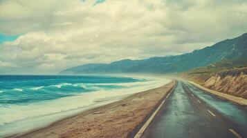 A scenic coastal road bordered by waves and mountains under a cloudy sky, inviting exploration and adventure. photo
