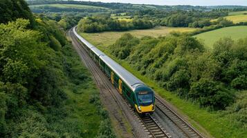 A train travels through lush green countryside, surrounded by trees and hills, showcasing a scenic railway journey. photo