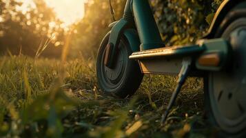 A close-up of a scooter resting on grass, illuminated by warm sunset light, surrounded by nature. photo