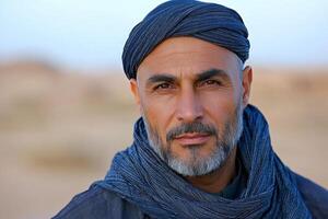 man wears dark blue jubba and taqiyah cap as he stands in beautiful desert setting wind softly moving his robe evoking sense of tradition and calm photo