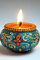 A beautifully decorated teal candle with intricate gold and maroon designs, glowing warmly against a simple background. photo
