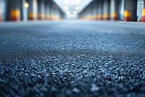Close-up of a textured asphalt surface in a dimly lit parking garage, featuring blurred yellow and red barriers in the background. photo