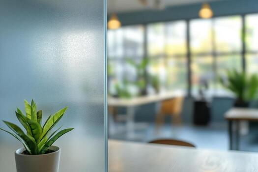 A small green plant in a pot with a blurred modern office background featuring large windows and natural light. photo