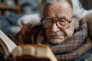 An elderly Caucasian man reads a book by the window, wrapped in a cozy scarf, with a thoughtful expression. photo