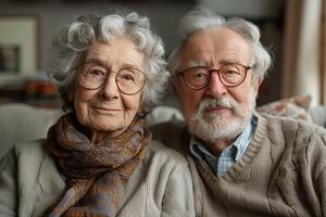 An elderly couple, Caucasian, with warm smiles and gray hair, sit together on a cozy couch in their home. photo