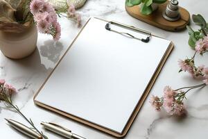 A serene workspace featuring a blank clipboard surrounded by soft pink flowers and elegant stationery. photo